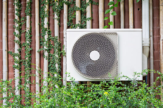 The air conditioner is mounted on the wall with the trees of the